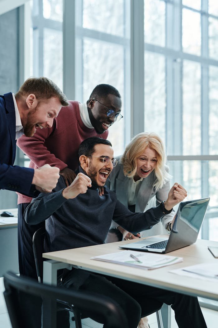 our-services-3 A diverse team in an office celebrates a successful achievement while looking at a laptop.